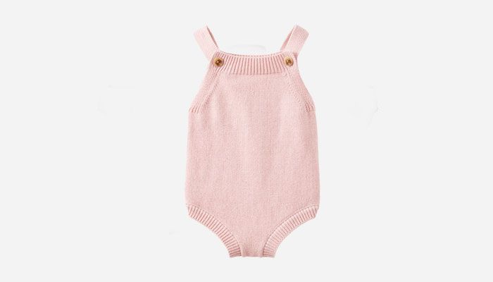 Pink knitted baby romper with shoulder straps and gold buttons on each strap